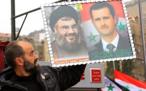 A Syrian man holds a picture of Hezbollah leader Hassan Nasrallah (L) next to Syrian President Bashar Al-Assad (R).