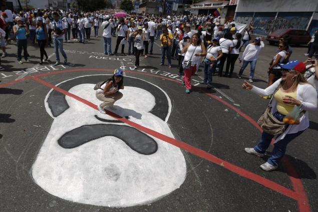 An opposition protestor poses over an anti-Maduro painting