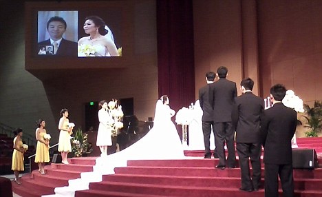 Bride Helen Oh stands alone at the altar as her husband-to-be Samuel Kim watches her from his isolation ward on the jumbo-sized screen. (Via)