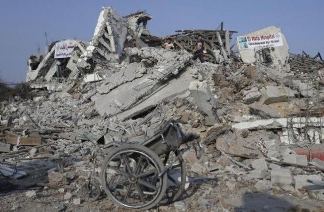 A wheelchair is seen as Palestinians stand atop the ruins of the headquarters of El-Wafa rehabilitation hospital, which witnesses said was destroyed during a seven-week Israeli offensive, in the east of Gaza City August 28, 2014. REUTERS/Ibraheem Abu Mustafa/Files