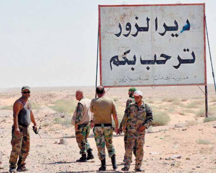 A group of soldiers at a sign saying Deir Ez-Zor welcomes you.