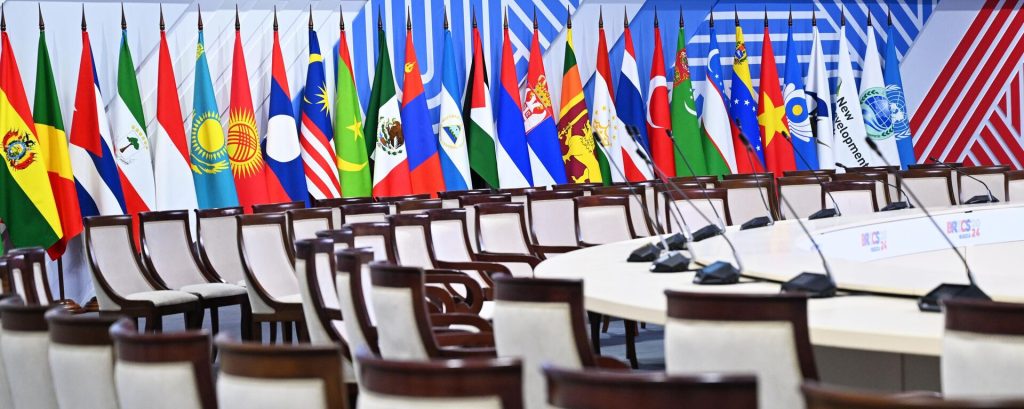 Display of BRICS countries' flags in an empty conference room.